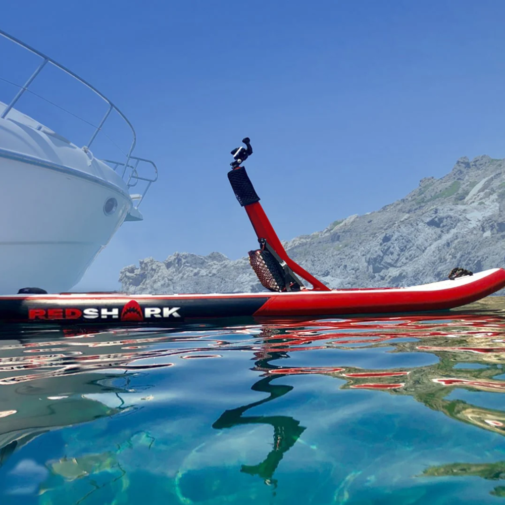 Red Shark Scooter Bike Surf besides a yacht in clear blue waters with mountains in the background.