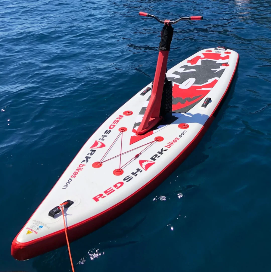 Red Shark Scooter Bike Surf parked on calm waters with reflection and clear blue sky.