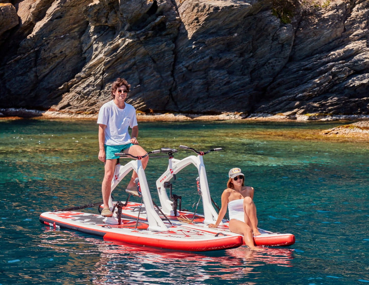 A couple using the Red Shark Tandem Surf Kit in the sea with cliffs in the background.