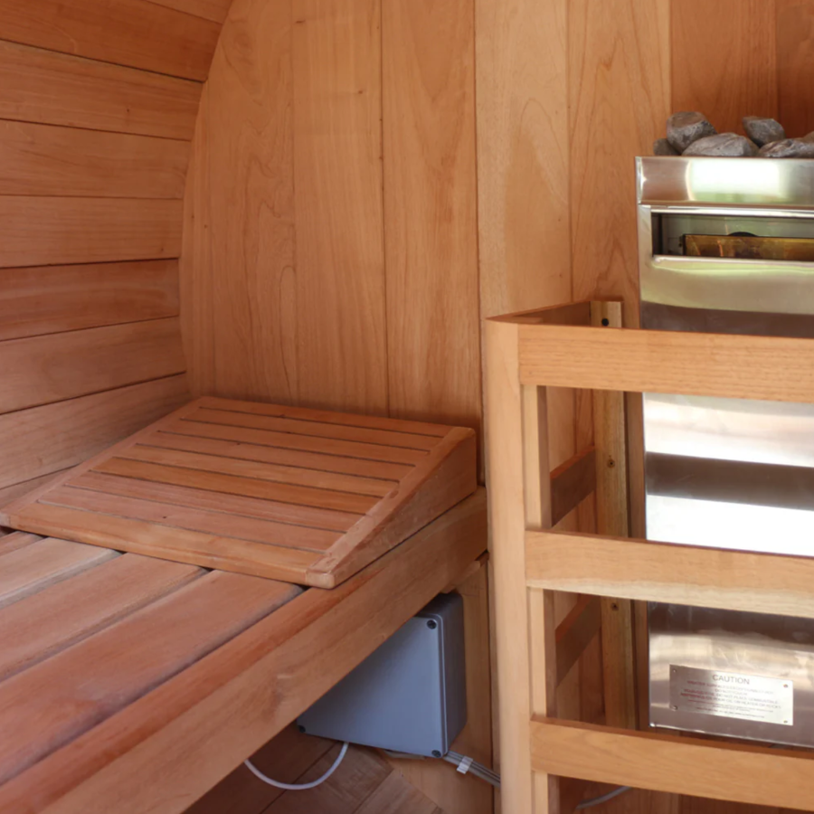 Inside view of Scandia Barrel Sauna with Canopy, showing the heater and the wooden bed.