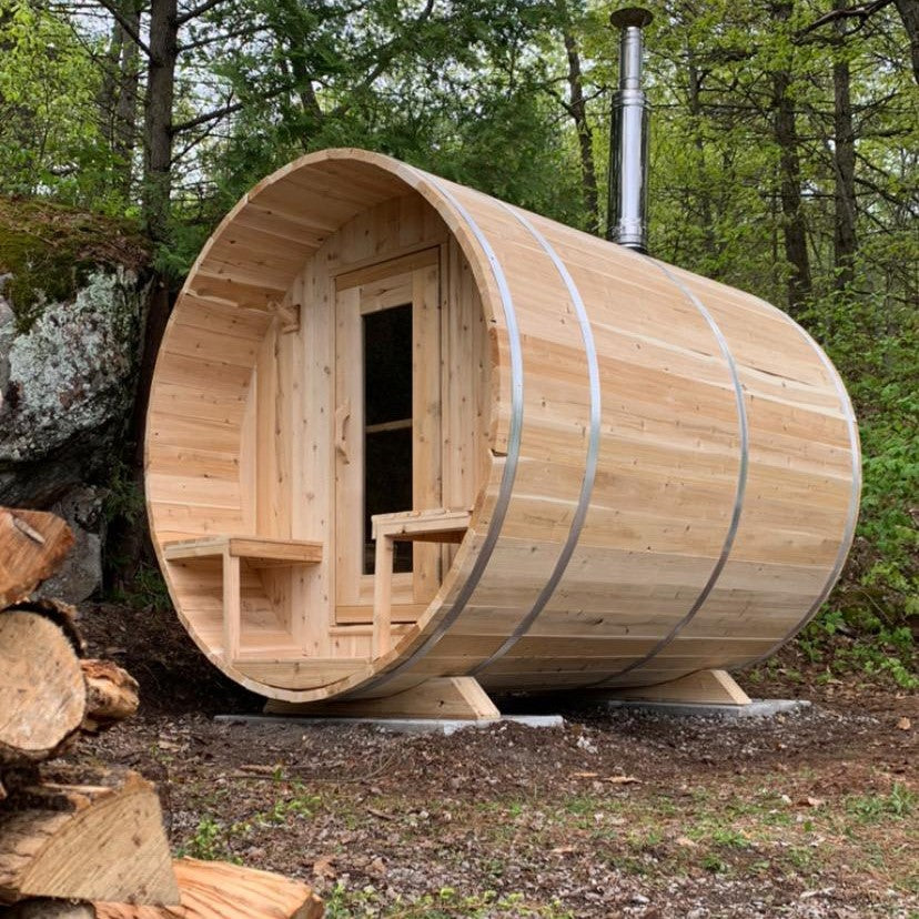 Leisurecraft Canadian Timber Outdoor Barrel Sauna in the middle of a forest with a wood-burning heater installed.