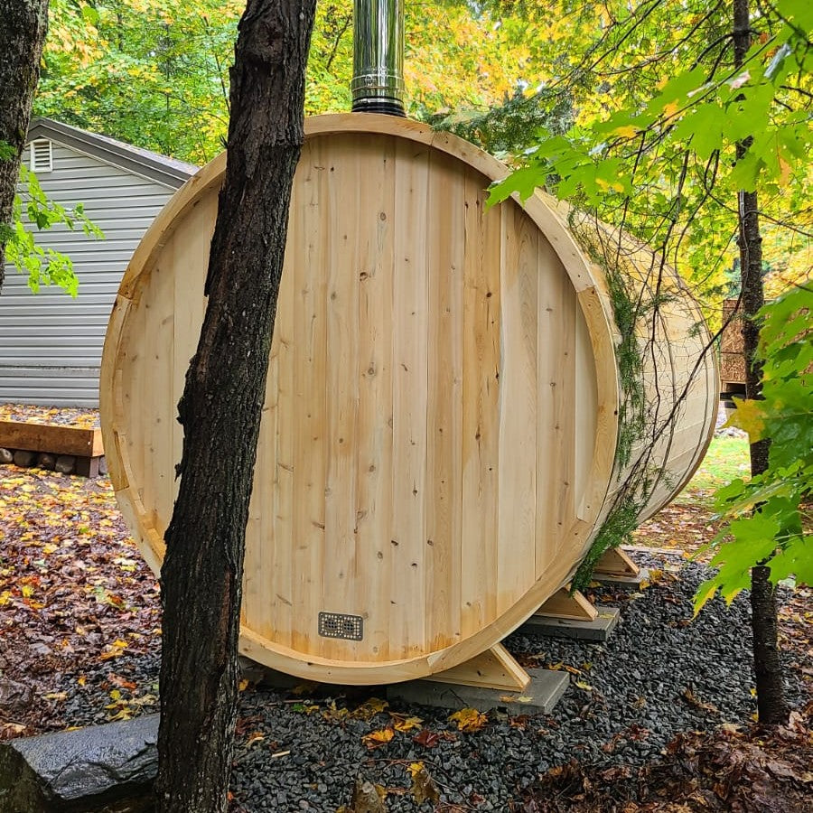 Back view of a Leisurecraft Canadian Timber Tranquility Outdoor Barrel Sauna in the middle of a forest. 