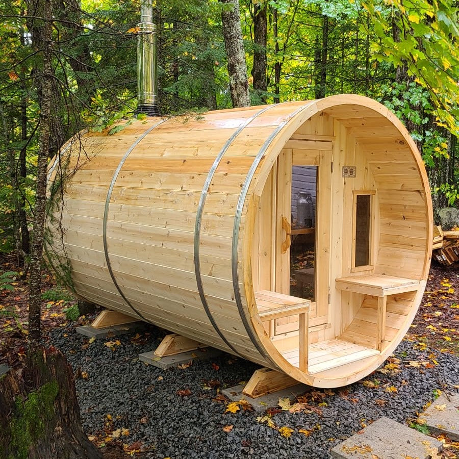 Leisurecraft Canadian Timber Tranquility Outdoor Barrel Sauna in the middle of the forest surrounded by nature and with a wood burning sauna heater installed.