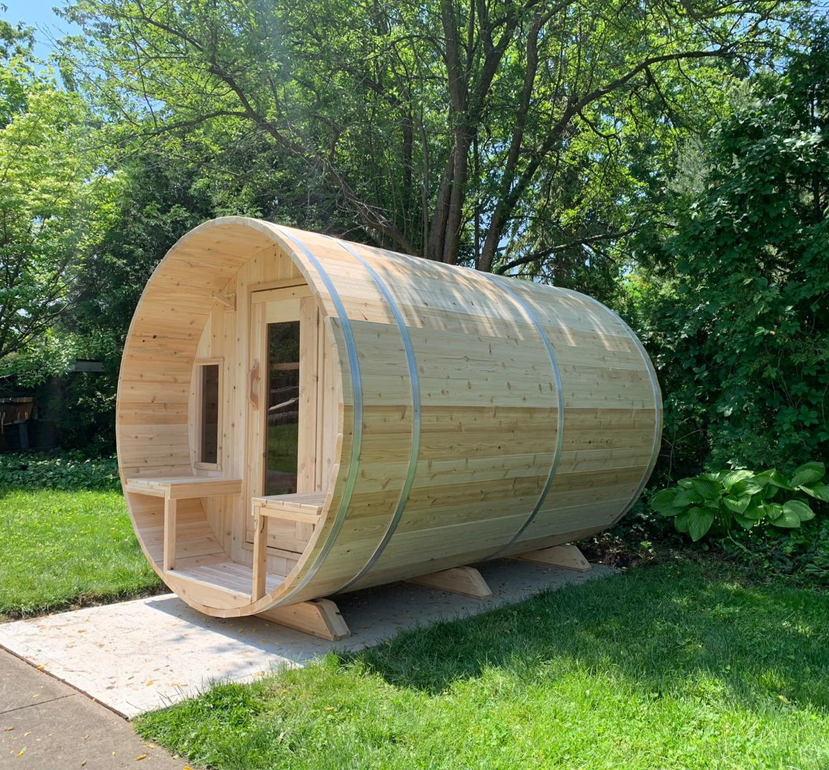 Leisurecraft Canadian Timber Tranquility Outdoor Barrel Sauna installed in a garden of a house during a sunny day.