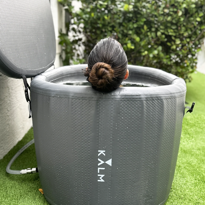 A woman using the Gray version of the Kalm Inflatable Cold Plunge Tub in an outdoor setting.